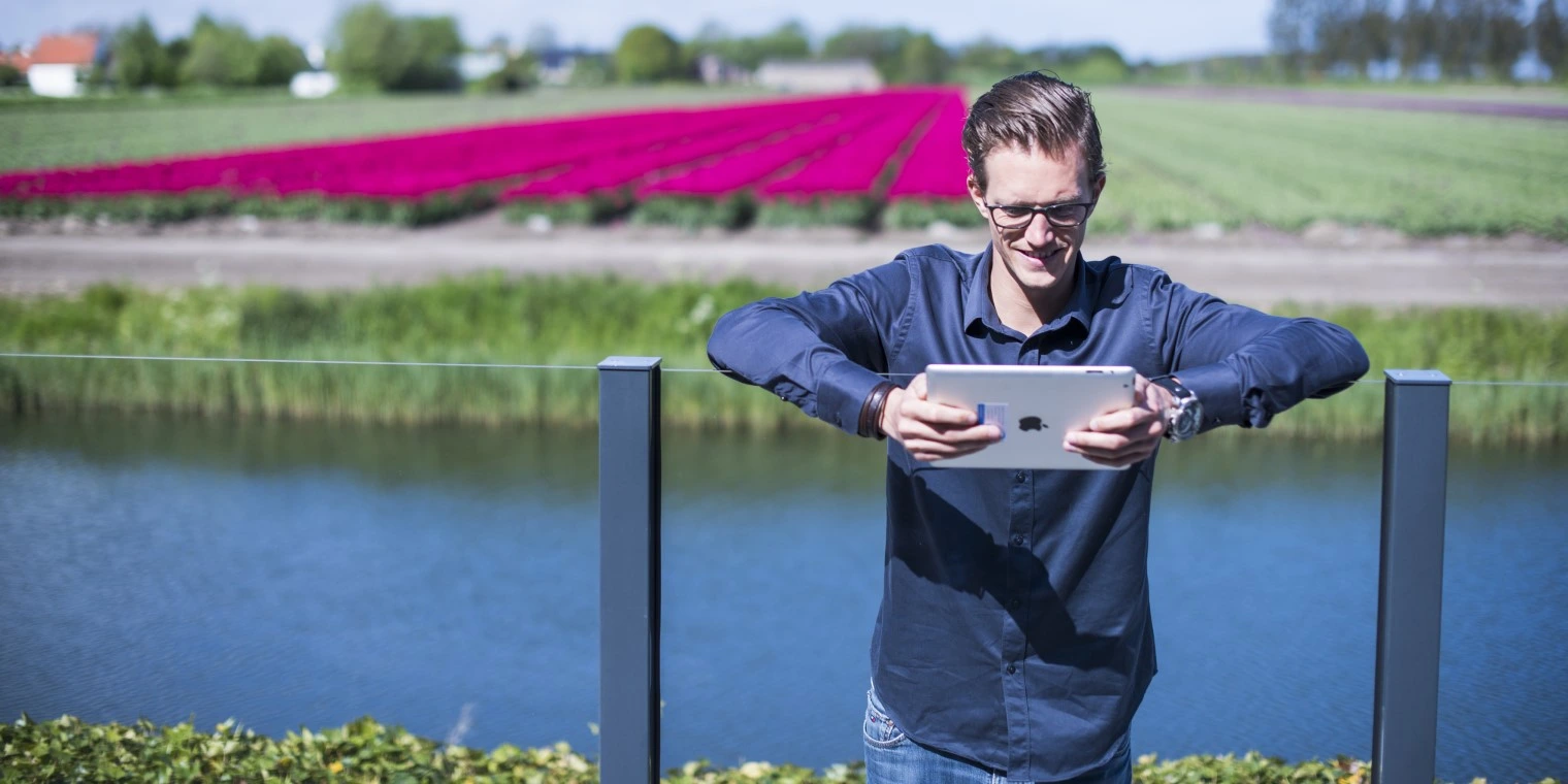 Mann steht am Fluß und sieht auf ein Tablet